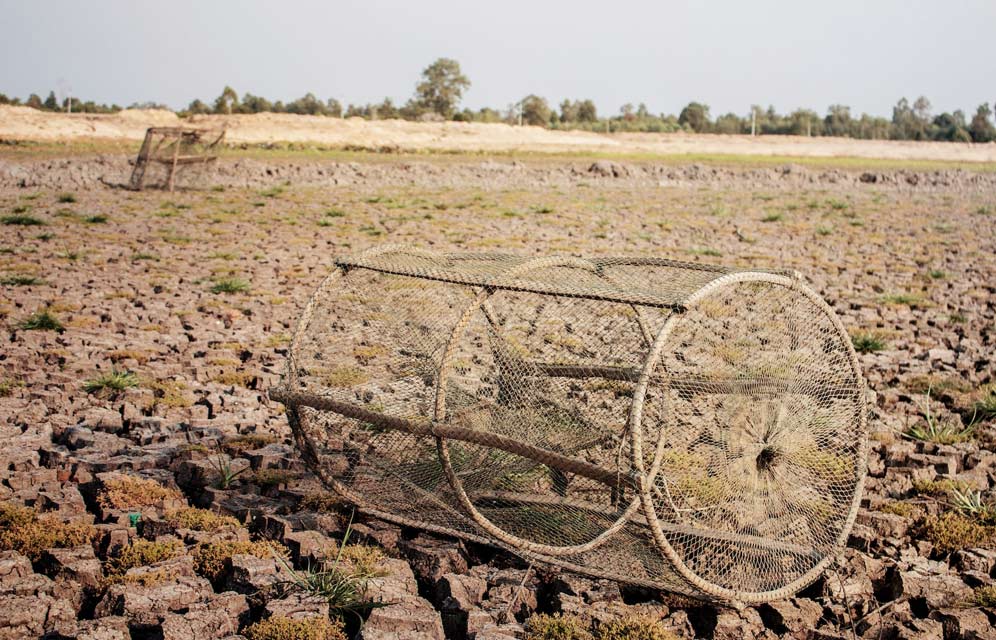 A cracked, dry lake bed with abandoned fishing traps, illustrating drought conditions and water scarcity.