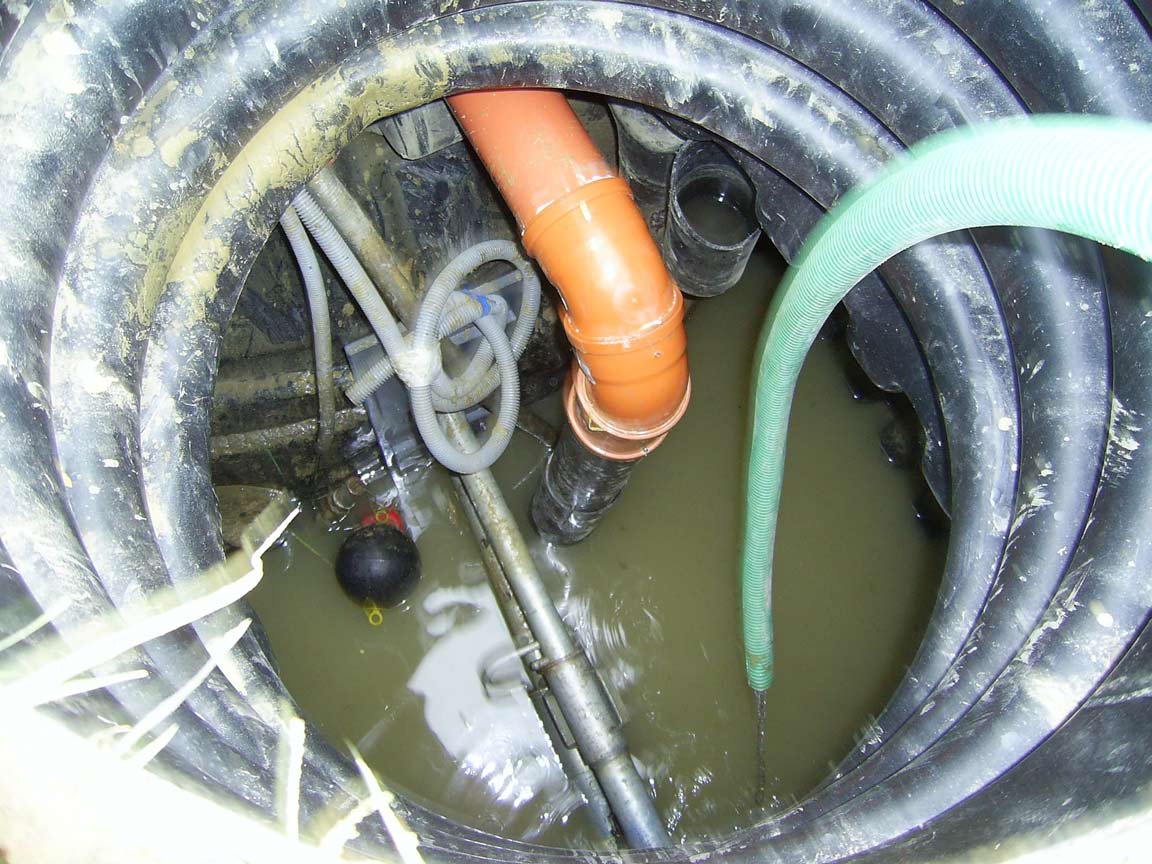 Inside view of a septic tank with sludge, orange pipes, and green hose for wastewater management.
