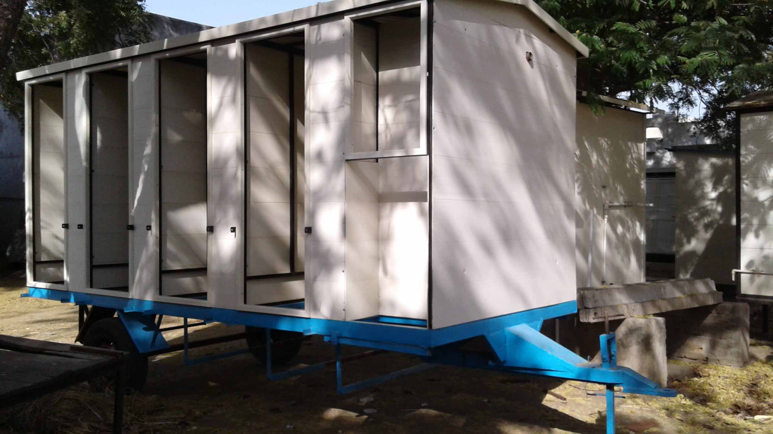 Portable toilet unit with multiple stalls at a construction site, shaded by trees.
